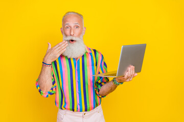 Portrait of impressed crazy granddad arm near open mouth use wireless netbook isolated on yellow color background