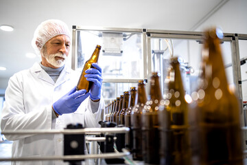 Beer production factory and experienced worker checking glass bottles before filling.
