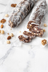 Obraz na płótnie Canvas Chocolate salami filled with almonds, hazelnuts and raisins on the white background. Chocolate sweet sausage shaped dessert sprinkled with powdered sugar. Christmas and New Year festive pastry