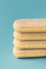 Fototapeta premium Traditional Italian savoiardi ladyfinger cookies stacked together on a blue pastel background. A pile of sweet sponge biscuits for tiramisu cake