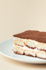 Homemade tiramisu cake on white plate against beige background. Traditional Italian no-bake dessert made of savoiardi, filled with mascarpone cheese, coffee espresso and sprinkled with cocoa powder