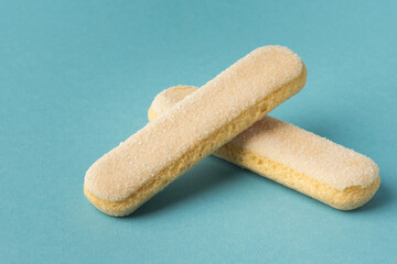 Traditional Italian savoiardi ladyfinger cookies stacked together on a blue pastel background. A pile of sweet sponge biscuits for tiramisu cake