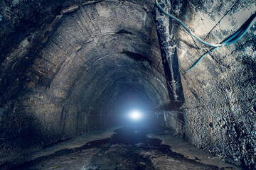 Sewer water in big underground sewage tunnel. Inside dark urban sewerage corridor tunnel with light...
