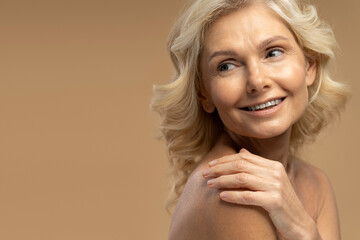 Closeup beauty portrait of smiling mature pretty woman looking away at copy ad space isolated on beige background. Concept of skin and body care. Aesthetic medicine. Anti-aging treatment 