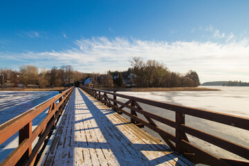 Fototapeta na wymiar Trakai lake covered with ice and a bridge in pleasant sunny cold winter day.