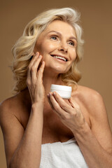 Advertising studio shot of caucasian attractive blonde mature woman, applying anti-aging smoothing...