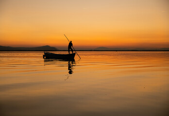 Sunset in Denizli Civril illuminated lake is approaching the shore with a fishing boat