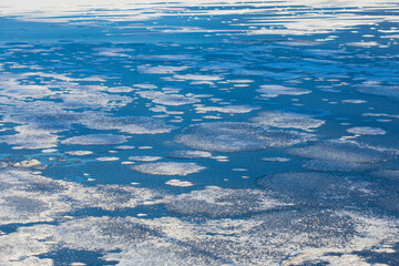 Ice floes on a blue lake water in sunny cold winter day. An abstract background texture photo.