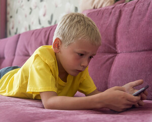 the boy is lying at home on the couch playing or chatting on a smartphone. natural light