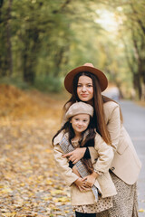 Portrait of happy mother and daughter spending time together in autumn park with falling yellow leaves