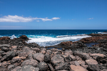 Fototapeta na wymiar Wild rocky coastline of Fuerteventura, Canary Islands, Spain. A big wave crashes on the rocks in rocky bay. Squirrels hiding among the rocks. Turquoise colors.