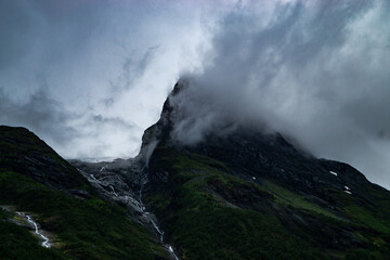 A cloud hangs on a hilltop. To the left of this is a glacier whose water flows down the mountain