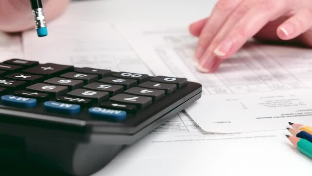 A hand holding a pencil makes calculations using a calculator. Close up of accountant or banker making calculations.