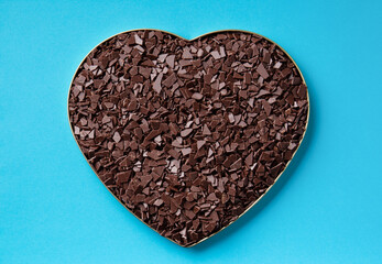 Dark chocolate in the shape of a heart on a blue background top view.