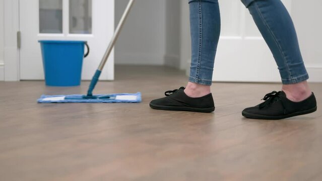 a woman cleans and mops the floor in the living room. The woman does housework.