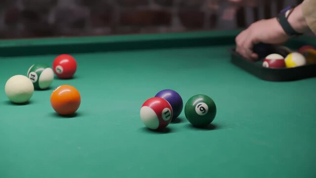 a man's hand collects colored balls after playing billiards and prepares a new game. spend free time