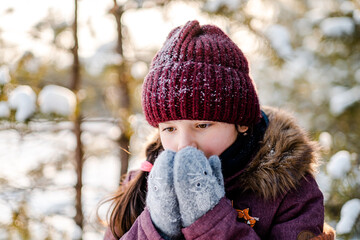A little girl on a walk in the winter forest sits and warms her hands. Fun walks during the winter holidays.