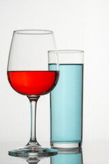 Vertical minimalist image of a glass and crystal glasses with colored drinks, and a white background
