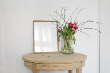 Blank wooden frame mockup. Spring bouquet of pink tulips and birch tree branches in glass vase...
