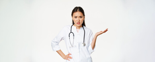 Confused asian woman doctor cant understand patient, looking puzzled and annoyed, raising hand up...