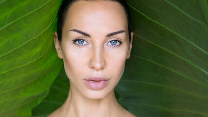 Beautiful Woman face with Natural nude make-up on a tropical leaf background. Healthy life. Purity