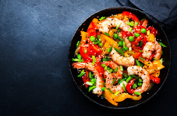 Stir fry with shrimps, red and yellow paprika, green pea, chives and sesame seeds in frying pan....