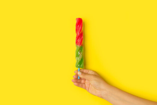Mano de mujer sosteniendo una paleta de helado natural y fresco sobre un fondo amarillo brillante liso y aislado. Vista de frente y de cerca. Copy space