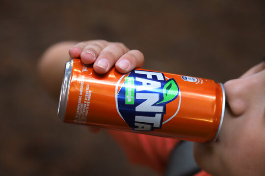 
Child having a soda. Boy drinking Fanta orange from a soda can. Aluminium can. Orange flavored drink. Recyclable container. Close up. Thirst. Can of Fanta in Spanish language.