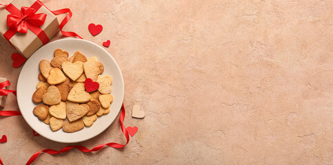 Fototapeta na wymiar Plate with sweet heart-shaped cookies and gift on beige background with space for text. Valentine's Day celebration