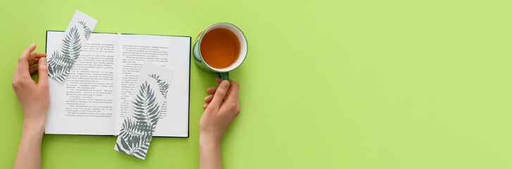 Female hands with book, cute bookmarks and cup of tea on green background with space for text