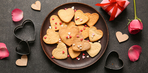 Plate of tasty heart-shaped cookies, flower and gift on dark background. Valentine's Day celebration