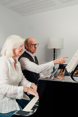 Older couple studying piano together and reading music sheet