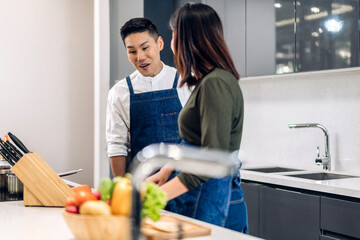Young asian family couple having fun cooking together and preparing salad with cook food on counter standing on table.Happy couple looking to preparing food in kitchen.