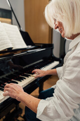 Older woman studying piano with music sheets on a grand piano