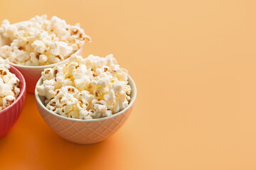 Bowls of delicious popcorn on color background