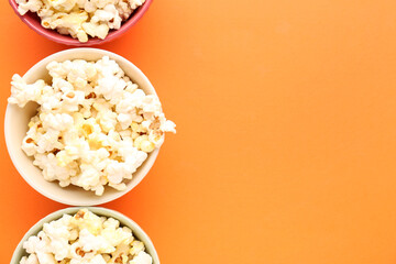 Bowls of delicious popcorn on color background