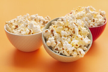 Bowls of delicious popcorn on color background