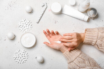 Female hands with cosmetic products and Christmas decorations on light background