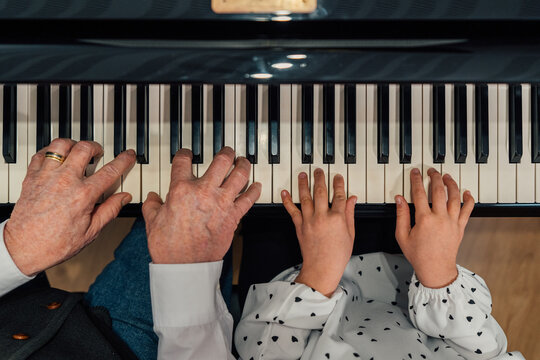 Close-up of senior piano student hands with her granddaughter playing the piano