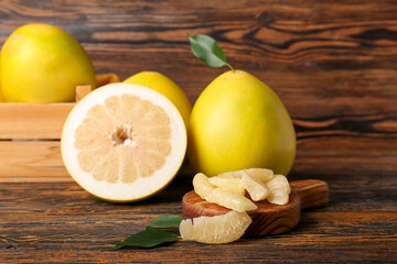 Wooden basket with whole and cut sweet ripe pomelo fruits on table