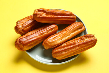 Plate with tasty eclairs on yellow background