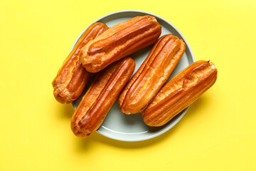 Plate with tasty eclairs on yellow background