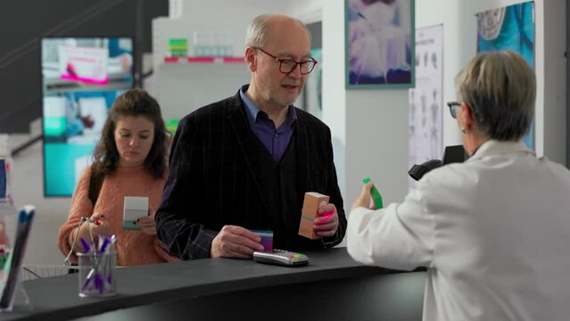 Senior client using credit card at pharmacy cash register counter to pay for prescription medicaments. Person buying pharmaceutical products at drugstore desk, pos terminal payment.