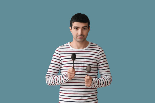 Young man with tablespoons on color background