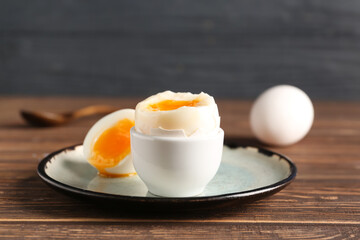 Plate with soft boiled egg on wooden table against black background