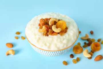Bowl with delicious rice pudding, different nuts, raisins and dried apricot on blue background
