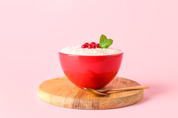 Board with bowl of delicious rice pudding, cranberries, mint leaves and spoon on pink background