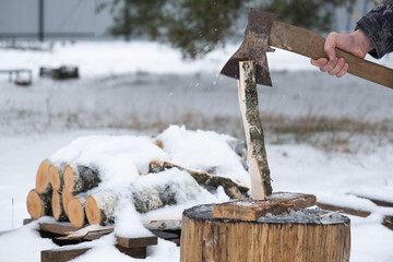 A man is chopping firewood with an axe in winter outdoor in the snow. Alternative heating, wood...