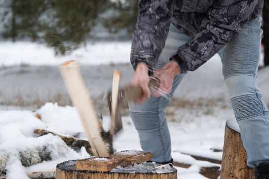 A man is chopping firewood with an axe in winter outdoor in the snow. Alternative heating, wood harvesting, energy crisis