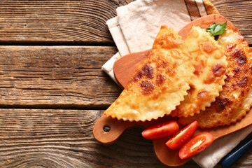 Cutting board with tasty chebureks and tomato slices on wooden background